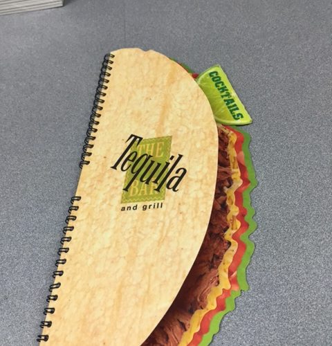 A coil bound menu with pages printed and cut to make the menu look like a taco.